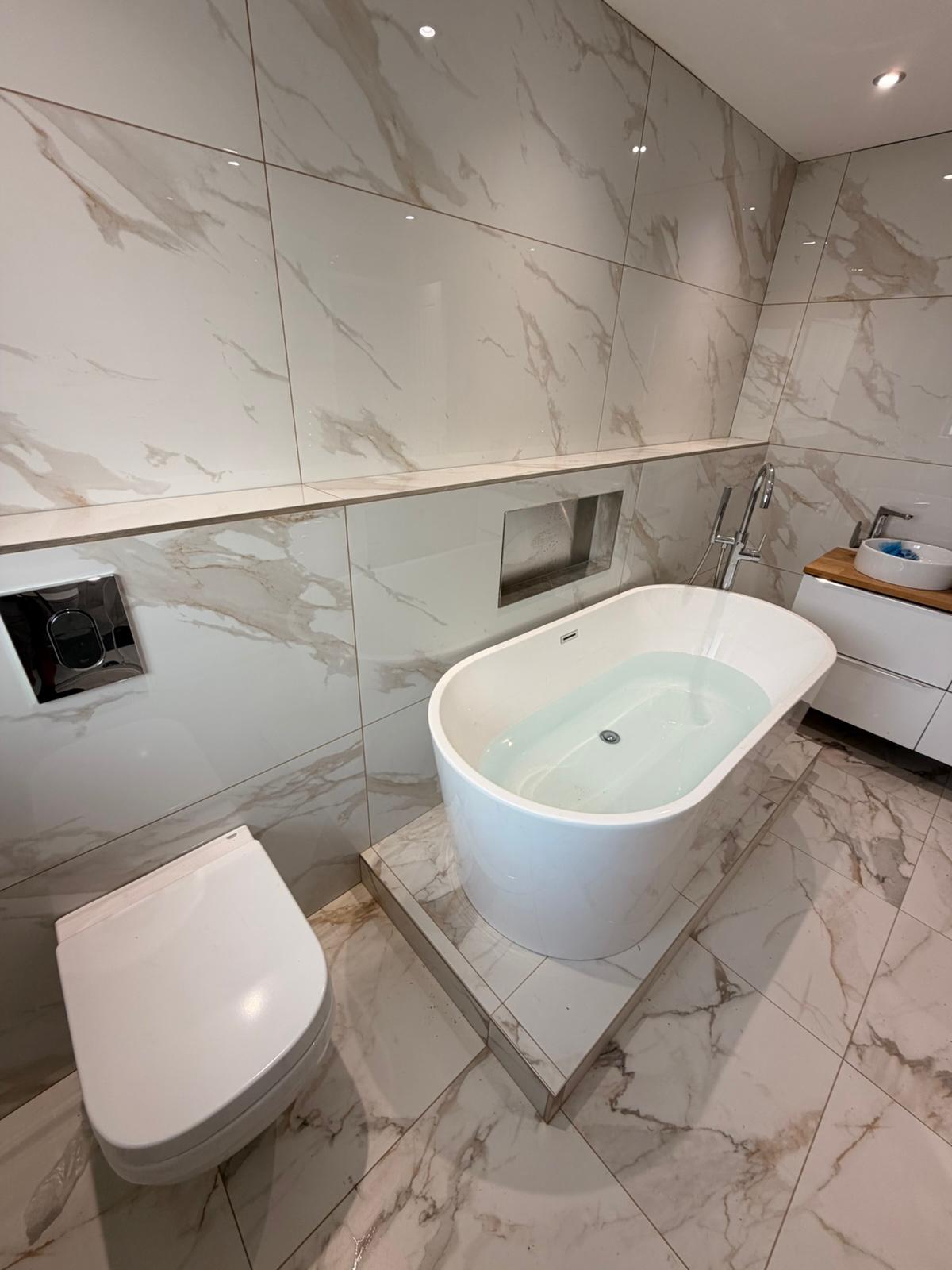 Marble bathroom with freestanding bath on a tiled plinth and wall-hung toilet